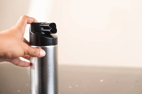 Tarafsız bir zemine karşı siyah bir hortumla metal sprey spreyi tutan bir el. Teneke kutunun parlak bir tasarımı var ve kullanıma hazır gibi görünüyor..