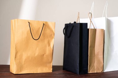 Tahta bir yüzeye yerleştirilmiş kahverengi, siyah ve beyaz da dahil olmak üzere çeşitli renklerde alışveriş torbaları. Çantaların farklı tasarım ve sapları var. Çeşitli stiller sergiliyorlar..