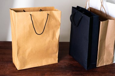Ahşap bir yüzeye yerleştirilmiş kahverengi, siyah ve beyaz da dahil olmak üzere çeşitli renklerde alışveriş torbaları. Çantaların sapları var ve kağıttan yapılmış, minimalist bir tasarım sergiliyorlar..
