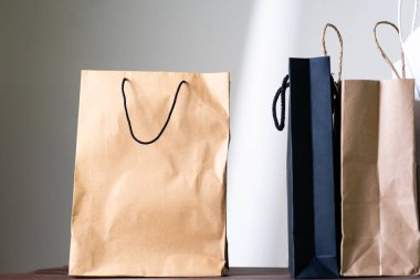 Kahverengi ve siyah da dahil olmak üzere çeşitli renklerde kağıt alışveriş torbaları, yumuşak ışıklandırmalı ahşap bir yüzeye yerleştirilmiştir..