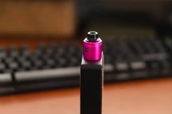 Siyah tabanlı pembe buhar cihazının yakın plan görüntüsü, bir klavye ve masanın bulanık arka planına göre ayarlanmış..