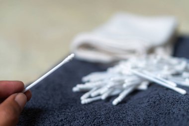 A close-up view of a pile of white cotton swabs scattered on a dark textured towel, with a soft cloth in the background. clipart