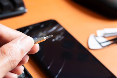 Birkaç bitli hassas bir tornavida seti, sarı bir alet tutacağı ve turuncu bir yüzey üzerinde çatlak bir ekranı olan akıllı bir telefon..