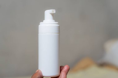 Beyaz bir pompa şişesini arka planda bulanık bir şekilde tutan kişi ürünün tasarımı ve basitliğini gözler önüne seriyor..