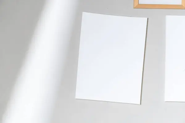 Açık gri bir yüzey üzerinde, arka planda kısmen görülebilen ahşap bir çerçeve bulunan boş beyaz bir sayfa..