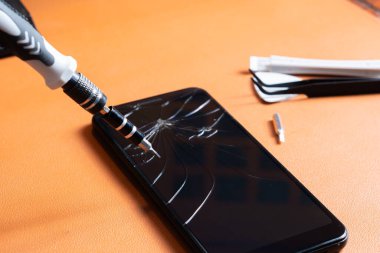 Birkaç bitli hassas bir tornavida seti, sarı bir alet tutacağı ve turuncu bir yüzey üzerinde çatlak bir ekranı olan akıllı bir telefon..