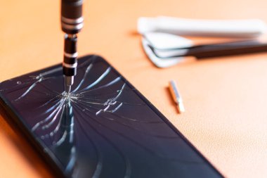 Birkaç bitli hassas bir tornavida seti, sarı bir alet tutacağı ve turuncu bir yüzey üzerinde çatlak bir ekranı olan akıllı bir telefon..