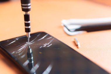Birkaç bitli hassas bir tornavida seti, sarı bir alet tutacağı ve turuncu bir yüzey üzerinde çatlak bir ekranı olan akıllı bir telefon..