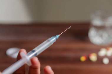 Dağılmış haplarla dolu ahşap bir masa, şırınga, ve açık bir hap şişesi, tıbbi ya da ilaç temalı.