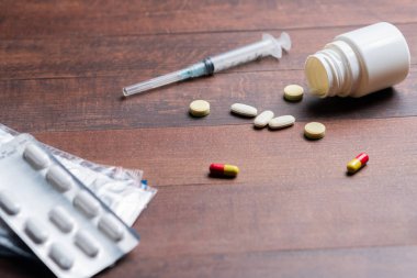 Dağılmış haplarla dolu ahşap bir masa, şırınga, ve açık bir hap şişesi, tıbbi ya da ilaç temalı.