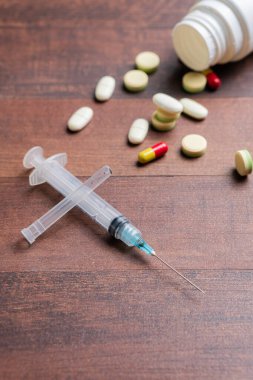 Dağılmış haplarla dolu ahşap bir masa, şırınga, ve açık bir hap şişesi, tıbbi ya da ilaç temalı.