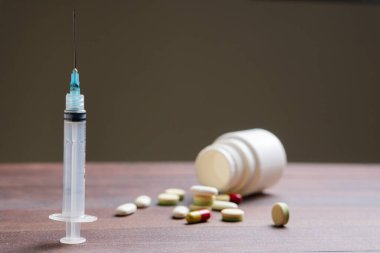 Dağılmış haplarla dolu ahşap bir masa, şırınga, ve açık bir hap şişesi, tıbbi ya da ilaç temalı.