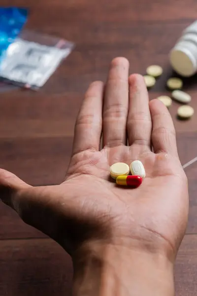 Elinde şırıngayla çeşitli haplar ve tahta bir yüzeye saçılmış daha fazla hap tutan bir el..