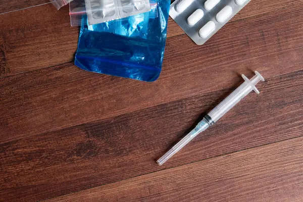 Bir şırınga ve ahşap bir zemin üzerinde çeşitli ilaç paketleri, sağlık, ilaç ve uyuşturucu kullanımının temalarını göstermektedir.