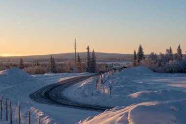 İsveç Laponya 'nın Kiruna kentindeki ormandan geçen kış yolu. Kuzey İskandinavya. Güneş doğduktan sonra çekilmiş..