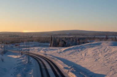 İsveç Laponya 'nın Kiruna kentindeki ormandan geçen kış yolu. Kuzey İskandinavya. Güneş doğduktan sonra çekilmiş..