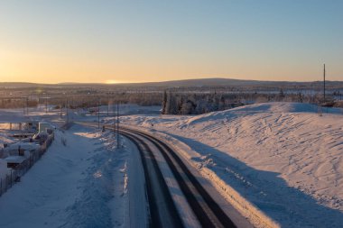 İsveç Laponya 'nın Kiruna kentindeki ormandan geçen kış yolu. Kuzey İskandinavya. Güneş doğduktan sonra çekilmiş..