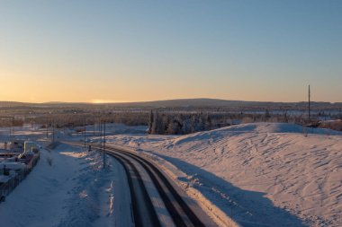 İsveç Laponya 'nın Kiruna kentindeki ormandan geçen kış yolu. Kuzey İskandinavya. Güneş doğduktan sonra çekilmiş..