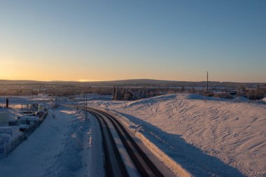 İsveç Laponya 'nın Kiruna kentindeki ormandan geçen kış yolu. Kuzey İskandinavya. Güneş doğduktan sonra çekilmiş..