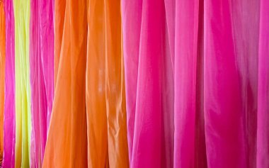 Neon yeşil, parlak turuncu ve canlı pembe renklerin uyumlu bir karışımına sahip akıcı renkli kumaş perdelerin yakın çekim görüntüsü hoş ve canlı bir atmosfer yaratıyor..