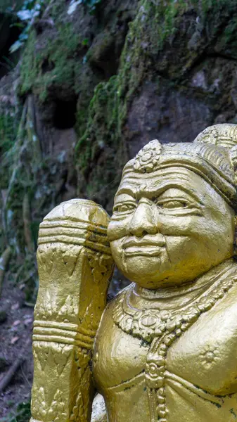 stock image Close-up of a golden Hindu statue in a serene natural environment with a moss-covered rocky background.