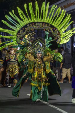 Yogyakarta, Endonezya-6 Ağustos 2025: Özenle hazırlanmış yeşil ve altın rengi geleneksel kıyafetlerle süslenmiş bir katılımcıyı gösteren canlı bir fotoğraf, kültürel bir sokak geçidi sırasında, mirası, yaratıcılığı,,