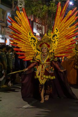 Yogyakarta, Endonezya-6 Ağustos 2025: Bir geçit töreninde altın aksanlı, dramatik kanatları ve kültürel mirası vurgulayan renkli geleneksel kıyafet. Yaratıcılığı, geleneği ve toplumu kutlayan canlı bir gece etkinliği sırasında yakalandı..