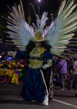 Yogyakarta, Endonezya-6 Ağustos 2025: Detaylı bir kostüm giymiş, altın aksanlı ve büyük tüylü kanatlı bir gösteri sanatçısı, kültürel bir kutlama sırasında bir gece gökyüzü altında dinleyicileri büyüledi..
