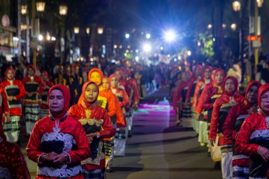Yogyakarta, Endonezya-6 Ağustos 2025: Geleneksel kırmızı giyinmiş bir grup kadın, aydınlanmış sokak lambaları altında, festival atmosferinin keyfini çıkaran bir kalabalığın içinde gece düzenlenen bir kültür geçidine katılıyor..