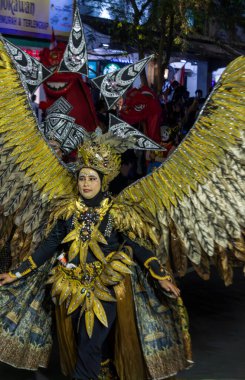 Yogyakarta, Endonezya-6 Ağustos 2025: Kültürel bir tören sırasında altın renkli, kuş esinlenilmiş bir kostüm giyen, sanatsal ifade, kutlama ve enerjik festival enerjisini somutlaştıran çarpıcı giyinmiş bir sanatçının dinamik görüntüsü.