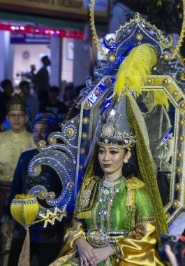 Yogyakar, Endonezya-6 Ağustos 2025: Kültürel bir gösteriye katılarak geleneksel bir kostüm ve başlık giymiş canlı bir karnaval sanatçısı. Diğer katılımcılar ise arka planda tamamlayıcı geleneksel kıyafetlerle görülüyor..