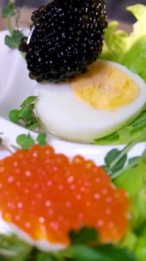 Ahşap zemin üzerinde kırmızı havyar olan haşlanmış tavuk yumurtasının yarısı. Yumurtanın üzerine siyah havyar koyun. Lezzetli ve sağlıklı yemekler servis etmek için.