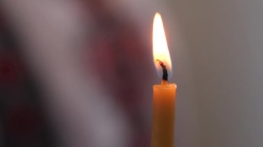 Yanan tek bir beyaz mum. Koyu arkaplanda yanan tek bir mum. Siyah arka planda sarı gölgeli beyaz parafin mum. Karanlıktaki Mum Işığı. Yüksek Çözünürlüklü Video Klipi.