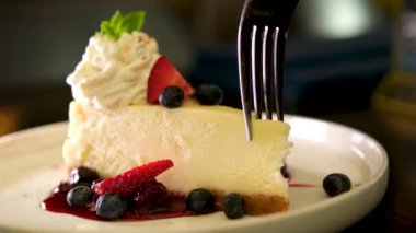 Cheesecake 'ten bir ısırık alıyorum. Klasik New York peynirli kek dilimi, çatalla yemek. New York peynirli keki, yaban mersini kremalı ve buruşuk çatallı lezzetli bir tatlı.