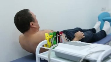 Bir kardiyolog hastaya kardiyogram yapar. Profesyonel doktorun kadın elleri modern klinikteki hasta adamı daha detaylı incelemek için kardiyogramı tutar. Tıptaki son teknolojiler. 
