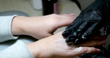 Siyah eldivenlerle kuaförde, kadın ellerine manikür üstüne krem sürme, cildin yenilenmesi prosedürü, cilt bakımı, bir kozmatolog, ellerin derisi. Yüksek kalite