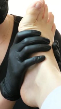 Profesyonel ayak masajı, pedikür salonunda ayak bakımı yapan siyah eldivenli kadın doktor ve maske, dairesel yoğurma hareketleriyle masaj yapıyor ayak tedavisi sorunları. pedikür salonu