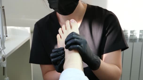 专业的足底按摩在修脚沙龙护理女医生的黑色手套和面具做按摩与圆形膝关节运动足部治疗问题的恢复 修脚沙龙 — 图库视频影像