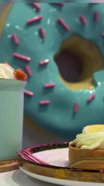 Pembe süslemeli kocaman mavi donutun arka planında içki ve tart olan bir kafe. Yüksek kaliteli FullHD görüntüler