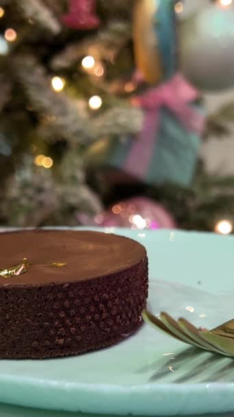 巧克力蛋糕放在蓝色的盘子里 背景是一棵新年圣诞树 背景上闪烁着彩灯 为您的广告金叉题词 — 图库视频影像