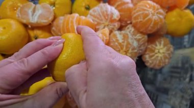Yeni yıl için mandalina soymak, pijamalı kadın, yakın plan, eller koyu ve sarı duvar kağıdı iştahlı C vitamininin arka planında lezzetli bir narenciye meyvesi soyar.