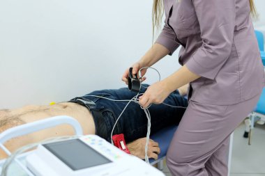 Bir kardiyolog hastaya kardiyogram yapar. Profesyonel doktorun kadın elleri modern klinikteki hasta adamı daha detaylı incelemek için kardiyogramı tutar. Tıptaki son teknolojiler. 