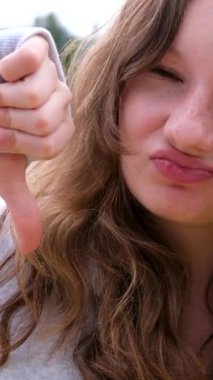 Dikey. Karşı duygular baş parmak göstererek memnuniyetsizlik seçeneğini geri çevirir. Sokaktaki genç, kahverengi saçlı, çilli, gülümseyen, kıvrık dudaklı, farklı duyguları olan spor ceketli.