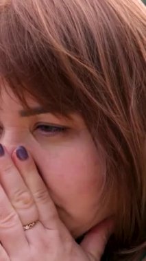 Yetişkin bir kadın göl kıyısındaki sokakta hapşırdığında bahar alerjilerine karşı alerjik bir reaksiyon omuz silkiyor kollarını yana açıyor yeşil ceketli kahverengi saçlı özür diliyor. Tombul güzel kadın..