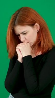 dikey video. Krom anahtar stüdyo duygularında yeşil arka planda olan kızıl saçlı genç bir kadın. Kahverengi gözlü, açık tenli, Avrupalı Amerikalı. Kanadalı. Genç sarışın kadın otururken stresli. 
