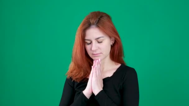 若い女性は 緑の背景に明るい赤い髪で祈りに彼女の手を折ります 高品質で — ストック動画