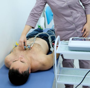 Bir kardiyolog hastaya kardiyogram yapar. Profesyonel doktorun kadın elleri modern klinikteki hasta adamı daha detaylı incelemek için kardiyogramı tutar. Tıptaki son teknolojiler. 