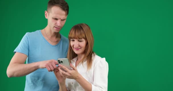 男性が緑色の背景に女性が自然の青いTシャツ白いジャケットライトの人々がタッチパッドのニュースフィードでオフィスで過ごすのを助ける問題を解決するためにインターネット上で電話で検索します ガジェット — ストック動画