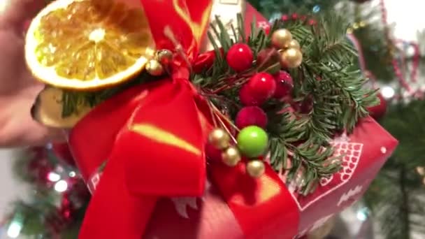 クリスマスツリーの近くに新しい年のギフトを包む愛する1つの工芸品の芸術のための赤い包装のクリスマスのギフトの美しいギフト ピースローワン スプルース 赤い弓 ドライフルーツ オレンジ ノート — ストック動画