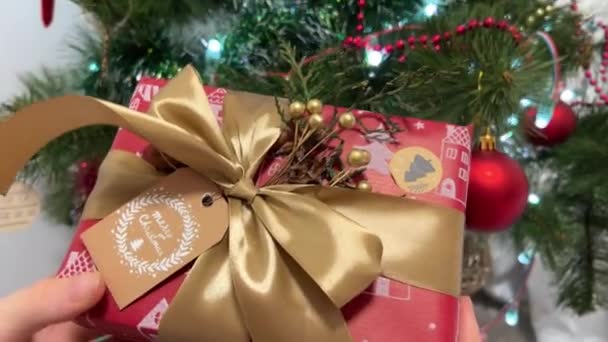 在圣诞树旁包装新年礼物用红色包装的漂亮礼物 上面有不同的装饰品 作为送给心爱的手工艺人的圣诞礼物 妇女包装圣诞礼物 — 图库视频影像